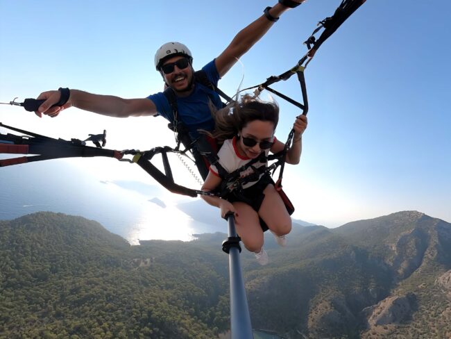 Ölüdeniz üzerinde Babadağ’dan tandem yamaç paraşütü uçuşu yapan bir turist, turkuaz deniz manzarası eşliğinde 2026 uçuş deneyimi.